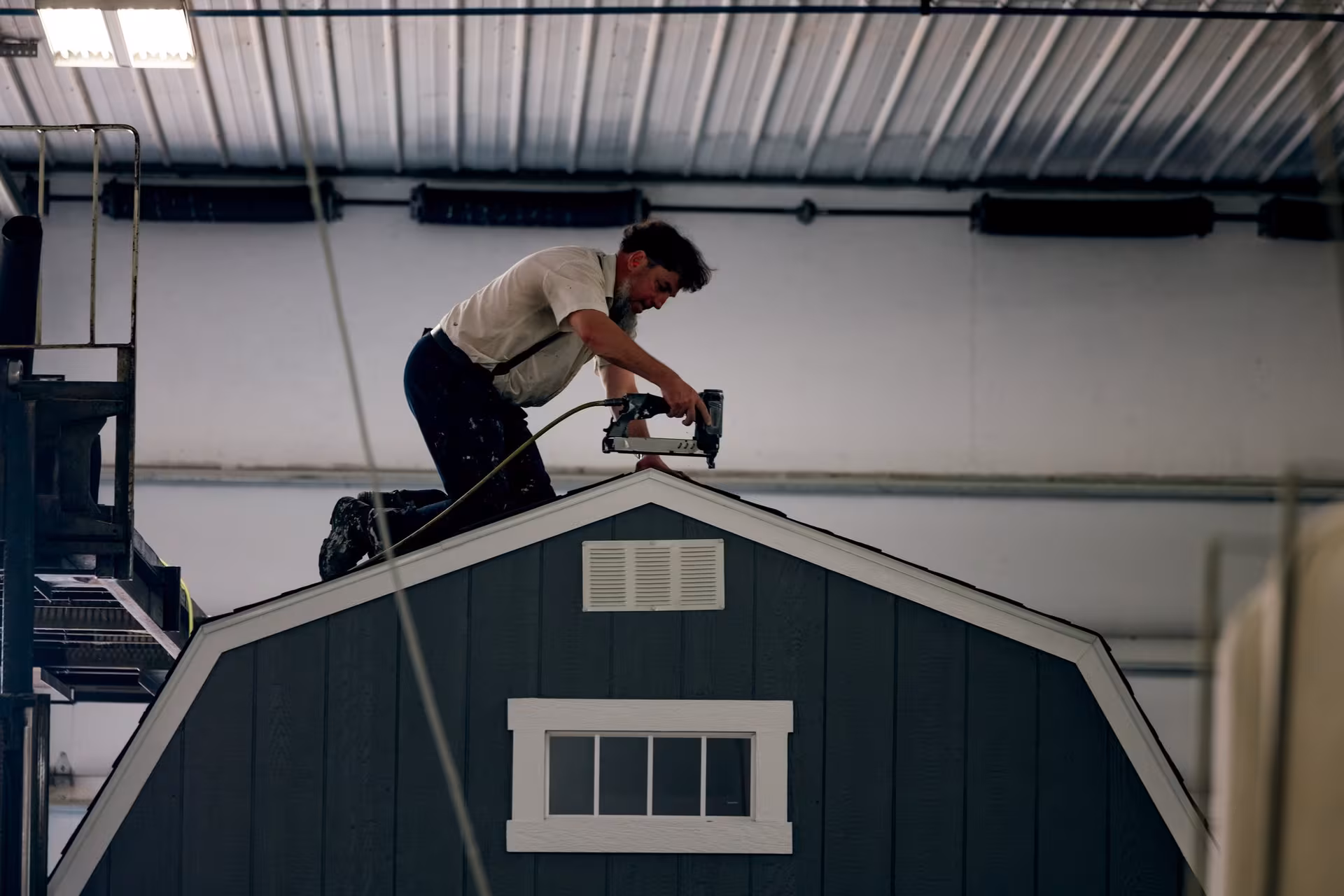 Amish builder hand-nailing a gambrel roof in the shop